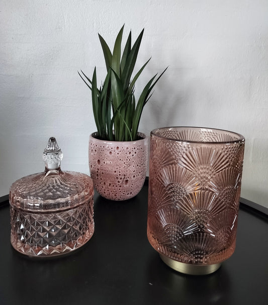 Led bordlampe rosa farvet med vifte møster. Lille glaskrukke i rosa farve. Lille kunstig bredbladet plante.