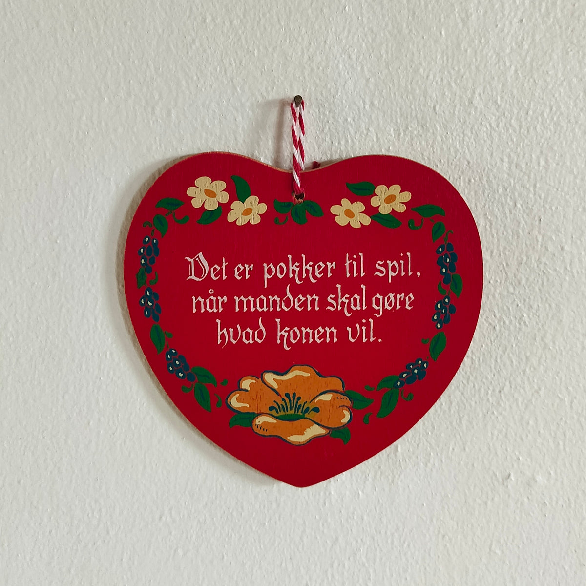 Lokumshjerte i rød med tekst: Det er pokker til spil, når manden skal gøre hvad konen vil.